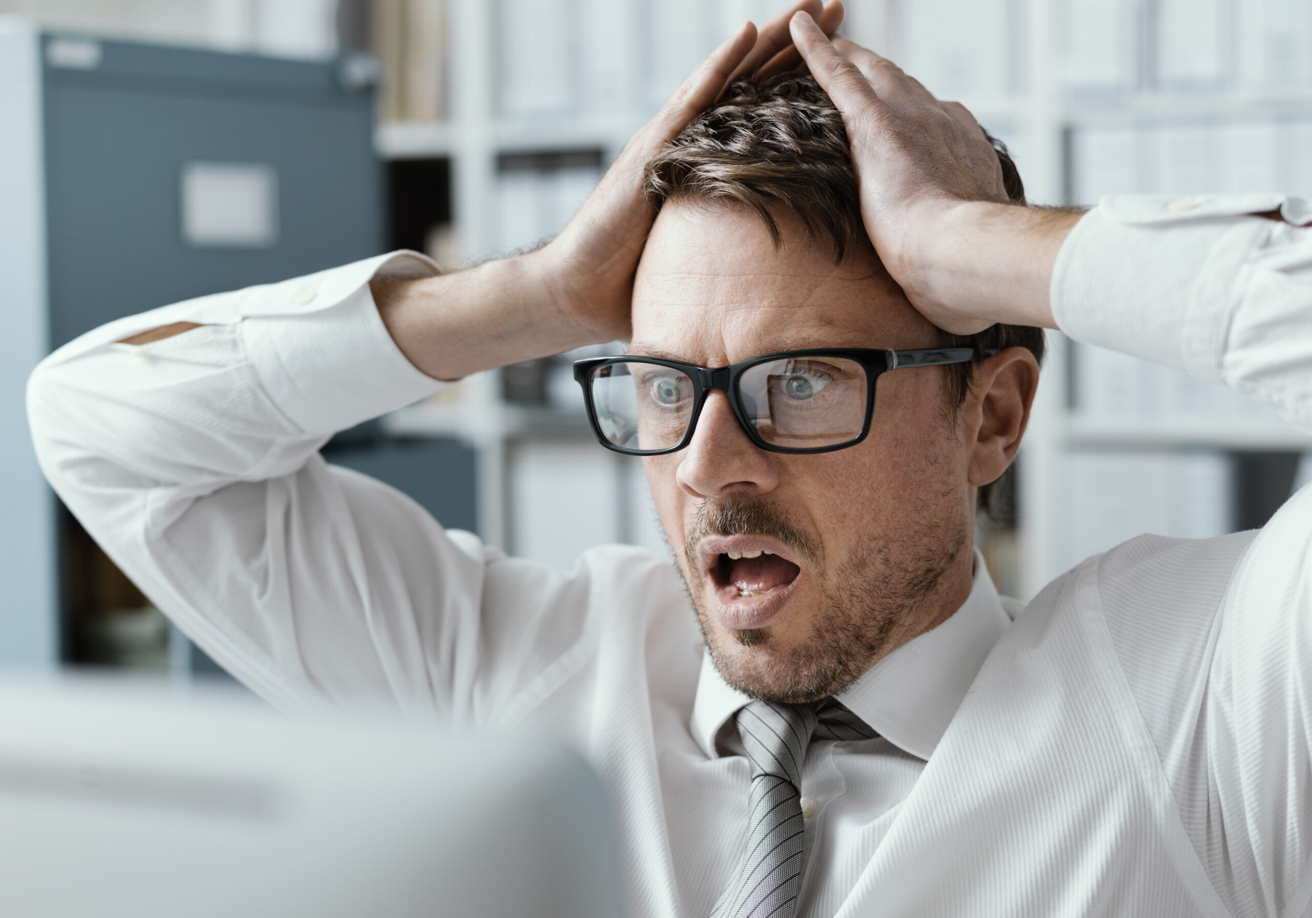 Panicking businessman with head in hands in his office, he is receiving shocking bad news on his computer